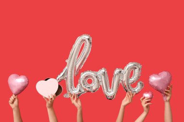 Hediye kutusu olan kadın elleri, sözcük şeklinde balonlar ve kırmızı arka planda kalpler. Sevgililer Günü kutlaması