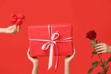 Hediye kutuları ve kırmızı arka planda kırmızı gül olan kadın elleri. Sevgililer Günü kutlaması