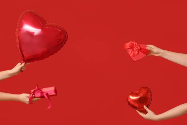 Kalp şeklinde balonları ve kırmızı arka planda hediye kutuları olan kadın elleri. Sevgililer Günü kutlaması