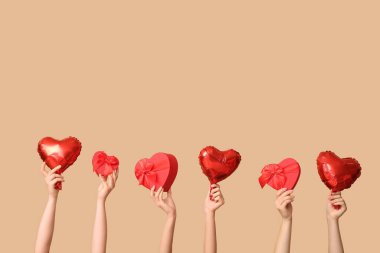 Hediye kutuları ve bej arka planda kalp şeklinde hava balonları olan kadın elleri. Sevgililer Günü kutlaması