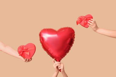Hediye kutularıyla kadın elleri ve bej arka planda kalp şeklinde hava balonu. Sevgililer Günü kutlaması