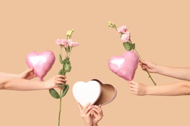 Hediye kutusu, çiçekler ve bej arka planda kalp şeklinde hava balonları olan kadın elleri. Sevgililer Günü kutlaması