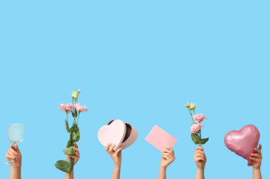 Kalp şeklinde balonu, zarfı, hediye kutusu, çiçekleri ve mavi arka planı olan kadın elleri. Sevgililer Günü kutlaması