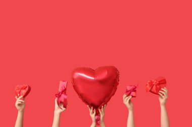 Hediye kutularıyla kadın elleri ve kırmızı arka planda kalp şeklinde balon. Sevgililer Günü kutlaması