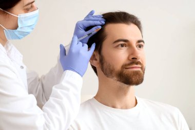 Kadın trikoloğun açık arkaplanda saç büyümesi için adama iğne yapması.