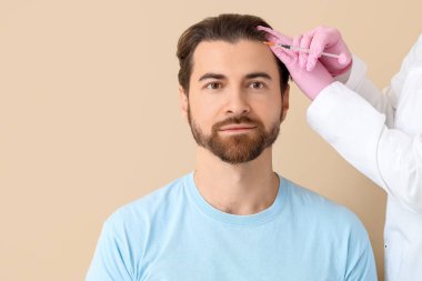 Yakışıklı genç adam bej arka planda saç büyümesi için iğne oluyor, yakın plan.