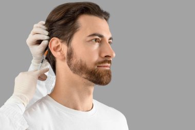 Yakışıklı adam gri arka planda saç büyümesi için iğne oluyor, yakın plan.