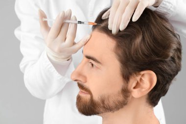 Yakışıklı adam gri arka planda saç büyümesi için iğne oluyor, yakın plan.