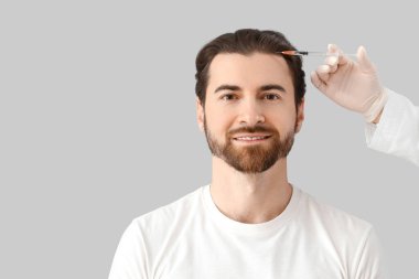 Genç adam gri arka planda saç büyümesi için iğne oluyor, yakın plan.