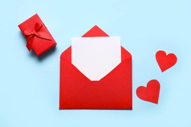 İçinde boş kart olan kırmızı bir zarf, hediye kutusu ve renkli arka planda kağıt kalpler. Sevgililer Günü kutlaması