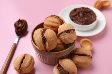 Tatlı ceviz şeklinde kurabiyelerle dolu bir kâse. Pembe arka planda kaynamış konsantre süt.