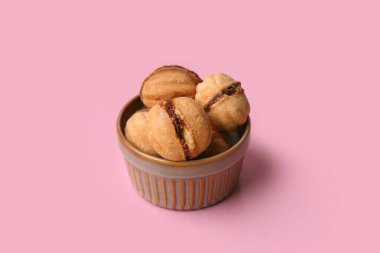 Tatlı ceviz şeklinde kurabiyelerle dolu bir kâse. Pembe arka planda kaynamış konsantre süt.