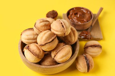 Ahşap kase ve ceviz şeklinde kurabiyeler, sarı arka planda kaynamış konsantre süt.