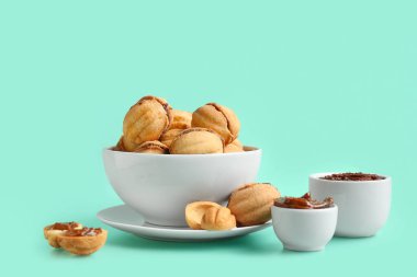 Bowl of sweet walnut shaped cookies with boiled condensed milk on turquoise background clipart