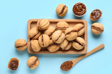 Ahşap tahta tahta üzerinde tatlı ceviz şekilli kurabiyeler ve mavi arka planda kaynamış konsantre süt.