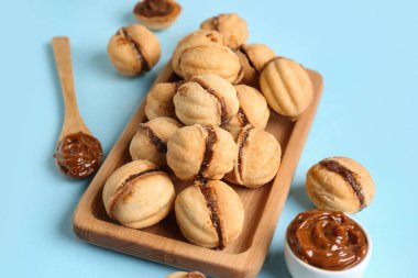 Ahşap tahta tahta üzerinde tatlı ceviz şekilli kurabiyeler ve mavi arka planda kaynamış konsantre süt.