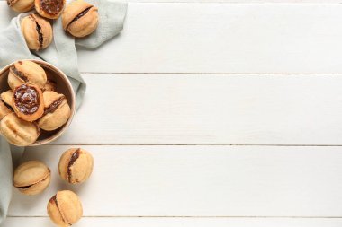 Beyaz ahşap arka planda kaynamış konsantre sütle ceviz şeklinde kurabiyeler.