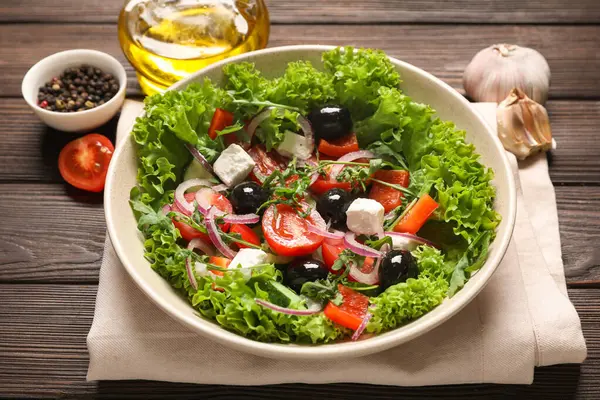 Bir kase lezzetli Yunan salatası ve ahşap masa malzemeleri.