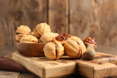 Tahta kesme tahtası ve bir kase tatlı ceviz şekilli kurabiye ve ahşap zemin üzerinde kaynatılmış konsantre süt.