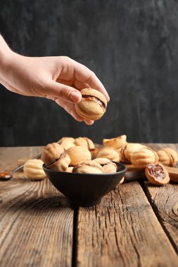 Female hand and bowl of sweet walnut shaped cookies with boiled condensed milk on wooden table clipart