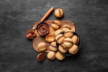 Wooden board and bowl of sweet walnut shaped cookies with boiled condensed milk on black background clipart