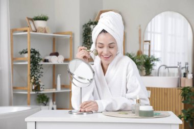 Güzel genç bir kadın banyodan çıktıktan sonra yüzüne aletle masaj yapıyor.