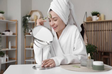 Güzel genç bir kadın banyodan çıktıktan sonra yüzüne aletle masaj yapıyor.