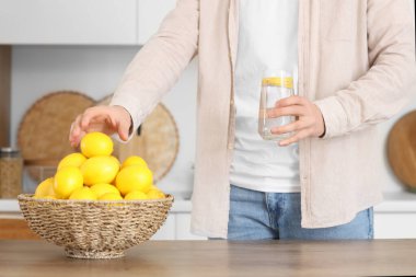 Genç adam bir bardak suyla mutfakta limon alıyor, yakın plan.
