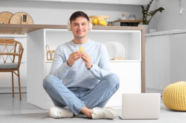 Kulaklıklı genç adam ve bir bardak limonlu su mutfakta oturuyor.