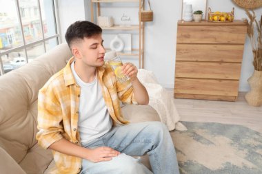 Evdeki kanepede oturan limonlu su dolu genç adam.