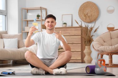 Evde paspasın üzerinde limonlu su dolu bir şişeyle oturan sportif genç adam.