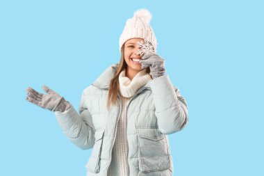 Mavi arka planda kar taneleri olan kışlık elbiseli genç bir kadın.