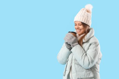 Mavi arka planda bir fincan kahveyle kışlık elbiseli genç bir kadın.