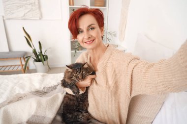 Güzel, mutlu, olgun, tatlı kedisi olan bir kadın evde selfie çekiyor.