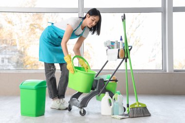 Kovası ve temizlik malzemeleriyle dolu bir vagonu olan kadın hademe.