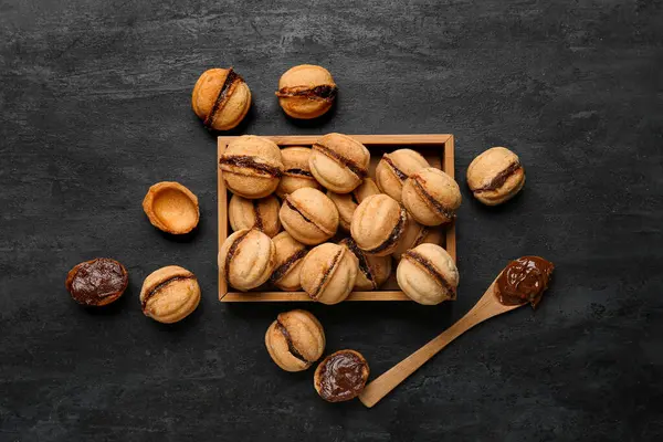 Ahşap kutu, tatlı ceviz şeklinde kurabiyeler ve siyah arka planda kaynamış konsantre süt.