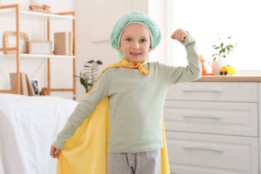 Klinikte süper kahraman peleriniyle kemoterapiden sonra küçük bir kız. Çocukluk kanseri farkındalığı