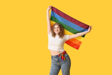 Sarı arka planda LGBT bayrağı olan mutlu genç bir kadın.
