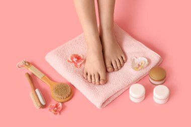 Güzel genç kadın, havlu, fırça, krem ve çiçeklerin bacakları pembe arka planda.