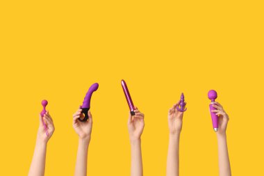 Vibratörlü kadın elleri, anal tıkaç ve sarı arka planda vajinal toplar.