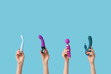 Mavi arka planda farklı vibratörlere sahip kadın elleri.