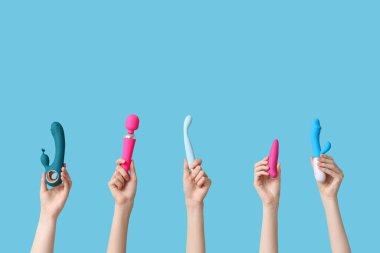 Mavi arka planda farklı vibratörlere sahip kadın elleri.