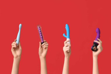 Kırmızı arka planda farklı vibratörlere sahip kadın elleri.