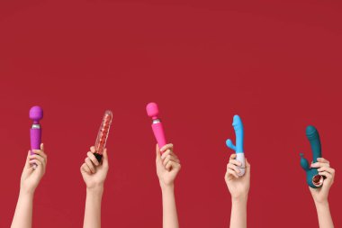 Kırmızı arka planda farklı vibratörlere sahip kadın elleri.