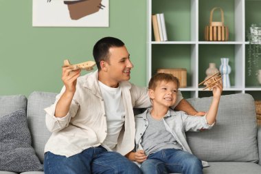 Mutlu baba ve küçük oğlu evdeki kanepede tahta uçaklarla oynuyorlar.
