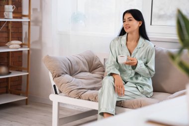 Mutfaktaki kanepede oturan bir fincan kahveyle genç bir kadın.