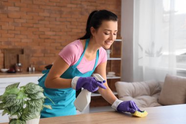 Genç bir kadın mutfakta süngerle masayı temizliyor.