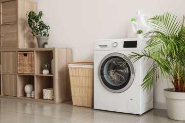 Çamaşır makinesi, sepeti ve raf ünitesi olan hafif çamaşır odasının içi.