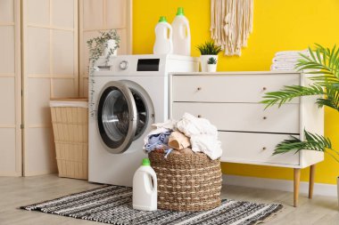 Kirli çamaşır, deterjan ve çamaşır makinesi. Odadaki sarı duvarın yanında.