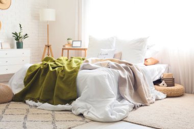 Buruşuk çarşaflı, komodinli, çekmeceli ve yatak odasının içinde lamba olan büyük, rahat bir yatak.